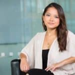 A professional Asian businesswoman sitting confidently in a modern office setting.