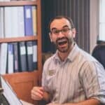 Man with glasses and beard looking excited while working at an office desk.