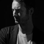 Dramatic side-lit black and white portrait of a man in a studio setting.