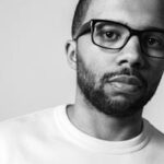 Close-up black and white portrait of a bearded man wearing glasses.