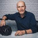 Bald man in a contemporary studio setting, smiling with a helmet, exuding confidence.